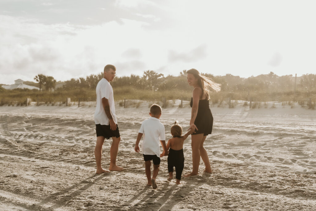 Family of four walking hand in hand along Myrtle Beach SC shoreline during sunset by Moody Momma photographer