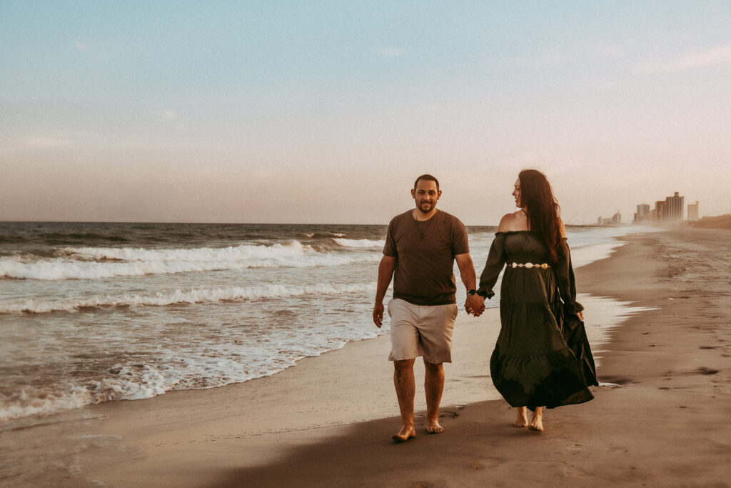 Couple holding hands walking along Charleston SC beach at sunrise captured by Moody Momma photographer